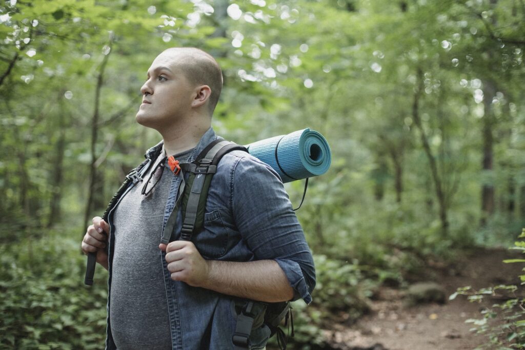 Male plump backpacker with hiking equipment in woods
